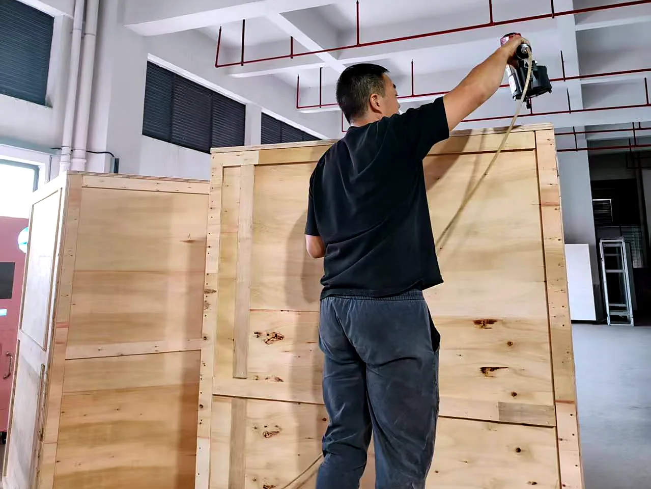 Factory worker sealing a plywood export crate around a pet washing machine
